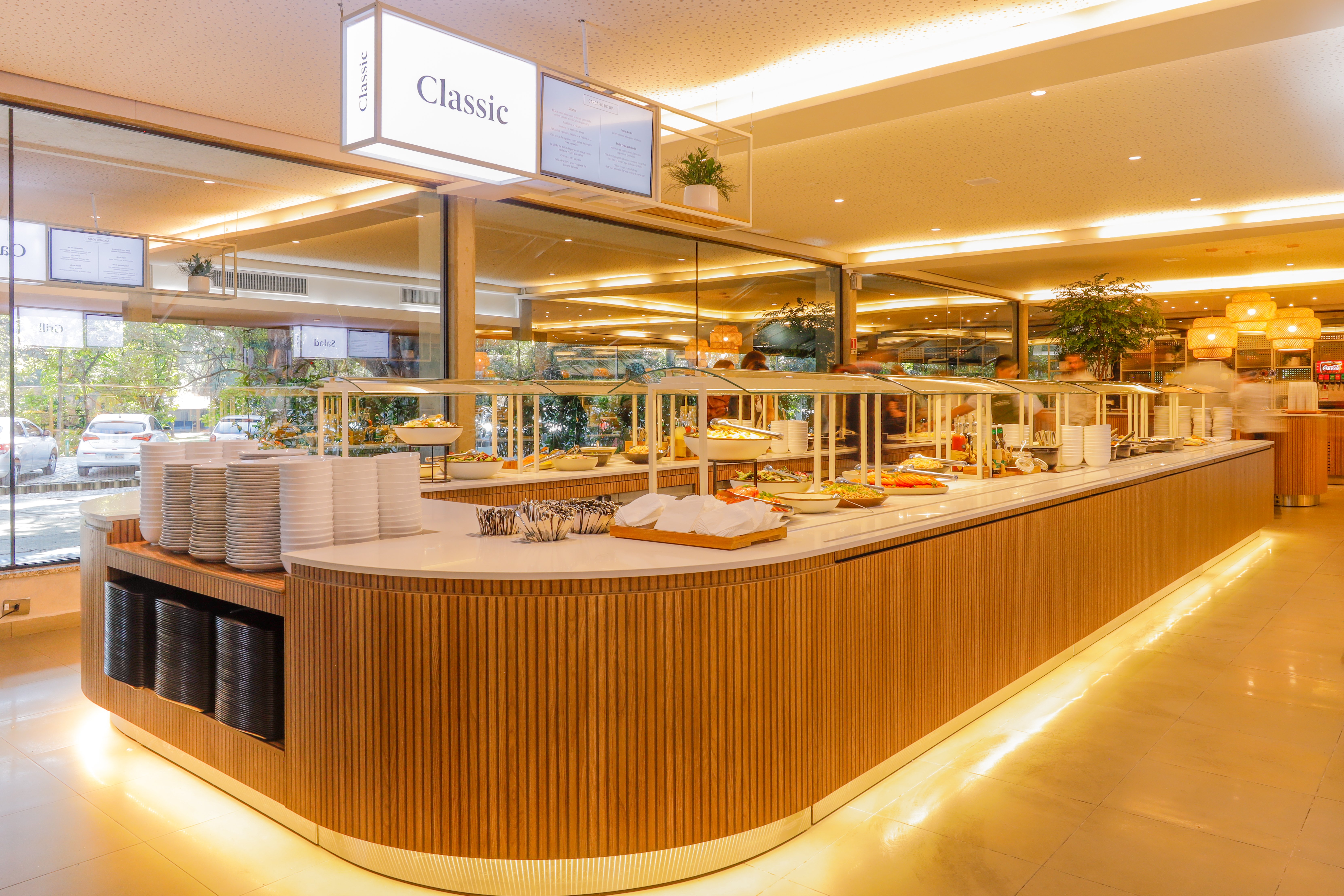 Buffet do Modern Recipe com ilhas de saladas e acompanhamentos, pilhas de pratos e estação sinalizada como “Classic” em restaurante corporativo iluminado. 