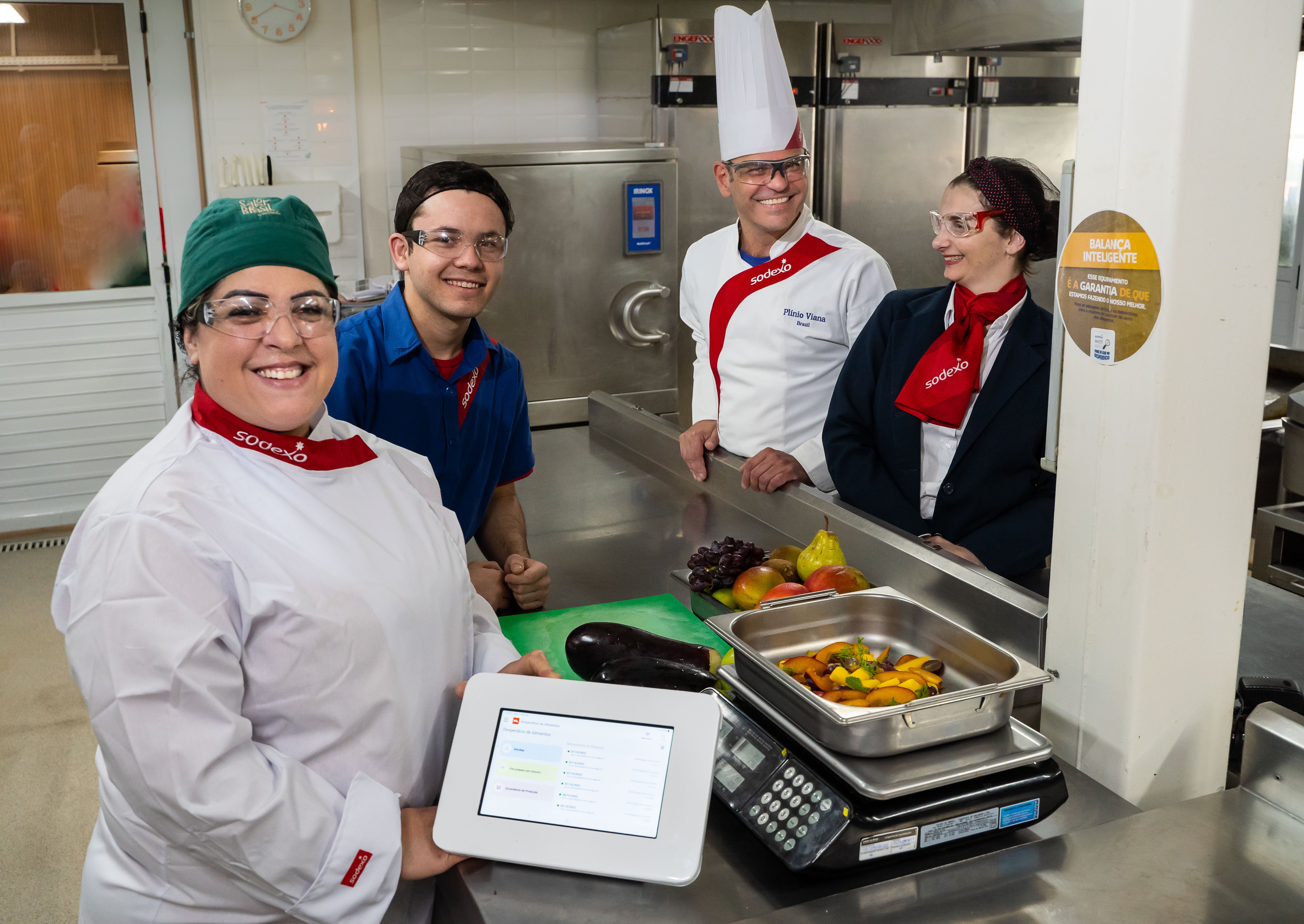  Colaboradores da Sodexo em uma cozinha industrial utilizam balança inteligente do programa WasteWatch para pesar alimentos, com tablet exibindo dados de monitoramento