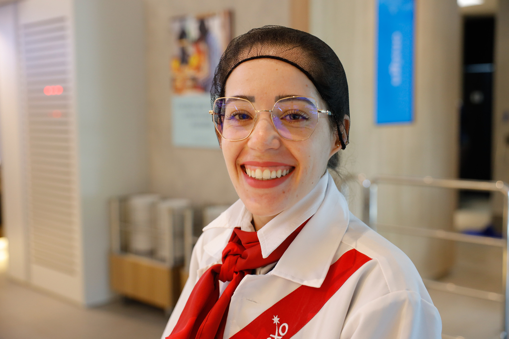 Colaboradora uniformizada sorri para a câmera em ambiente de restaurante corporativo.