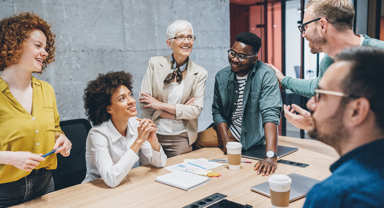 Team gathered around a conference table in a modern office, discussing ideas with notes, charts, and coffee cups spread across the workspace.