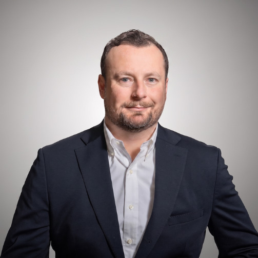 Kevin Booth headshot in a navy blazer and white shirt against a light gray background.