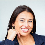 Tanya Cerniuk in a navy blazer and patterned shirt, seated indoors with hand resting on chin.