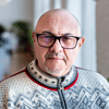 A bald man wearing glasses and a sweater, looking directly at the camera with a neutral expression.