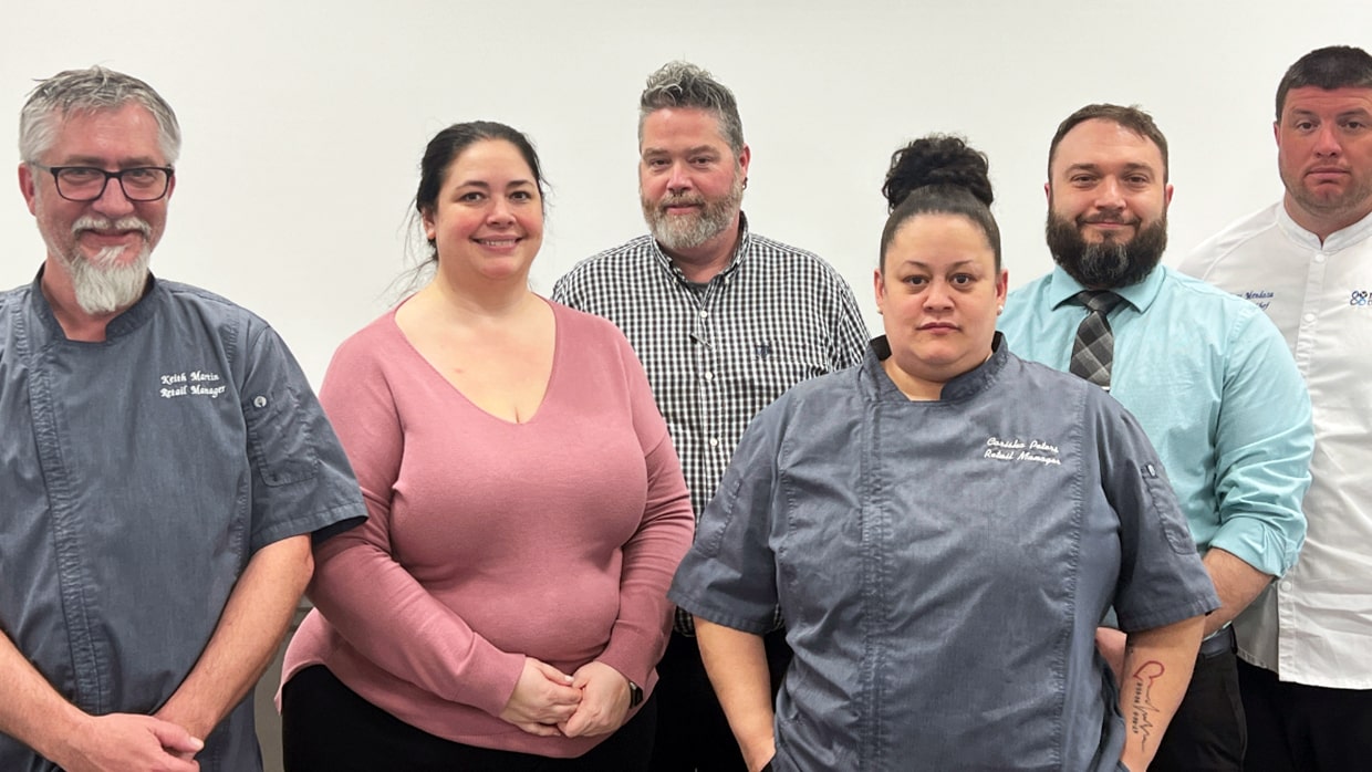 Six people standing together, some in chef uniforms and others in casual clothing, in a group setting.