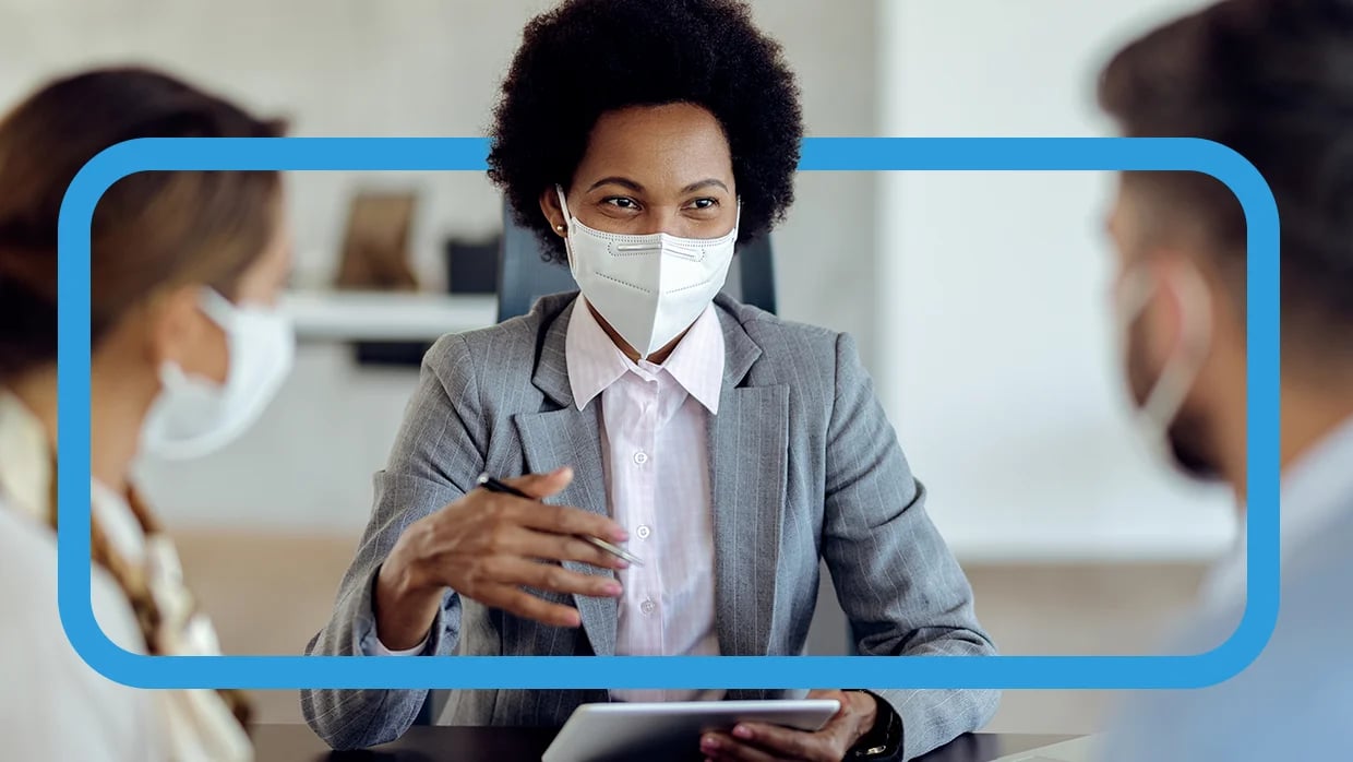 Person in suit shows tablet to masked pair in professional setting, discussing or presenting something.