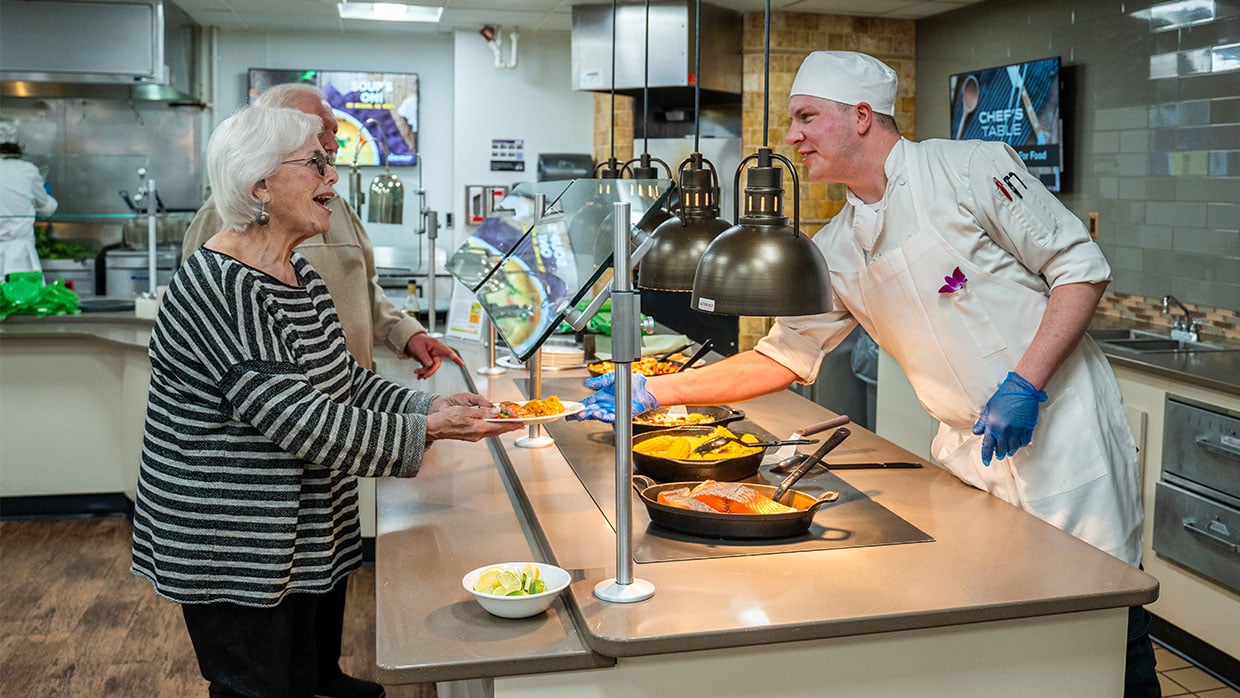 Chef serving a freshly prepared meal to a senior couple.