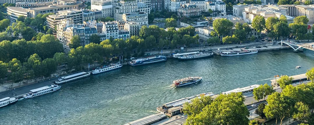A river with boats gliding on it, framed by a bustling city skyline in the background.