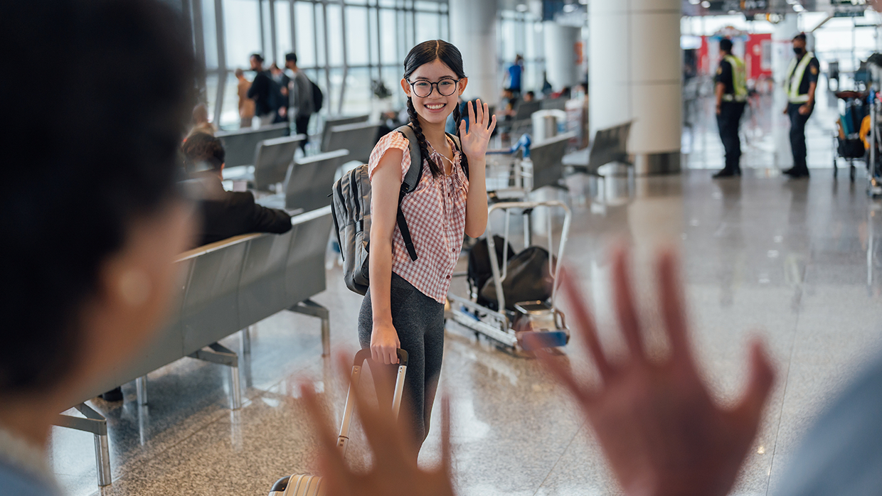 Young girl at an airport smiling and waving goodbye to her parents