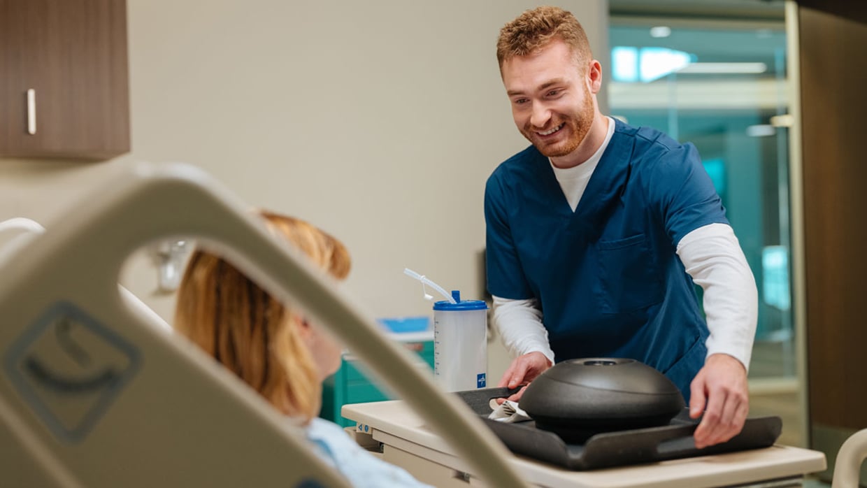 A smiling nurse serving food to a patient in a hospital room setting