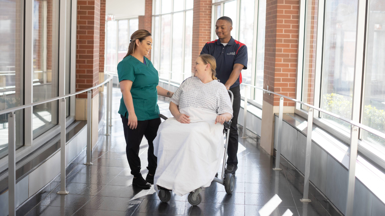 Hospital patient receiving assistance from two service employees.