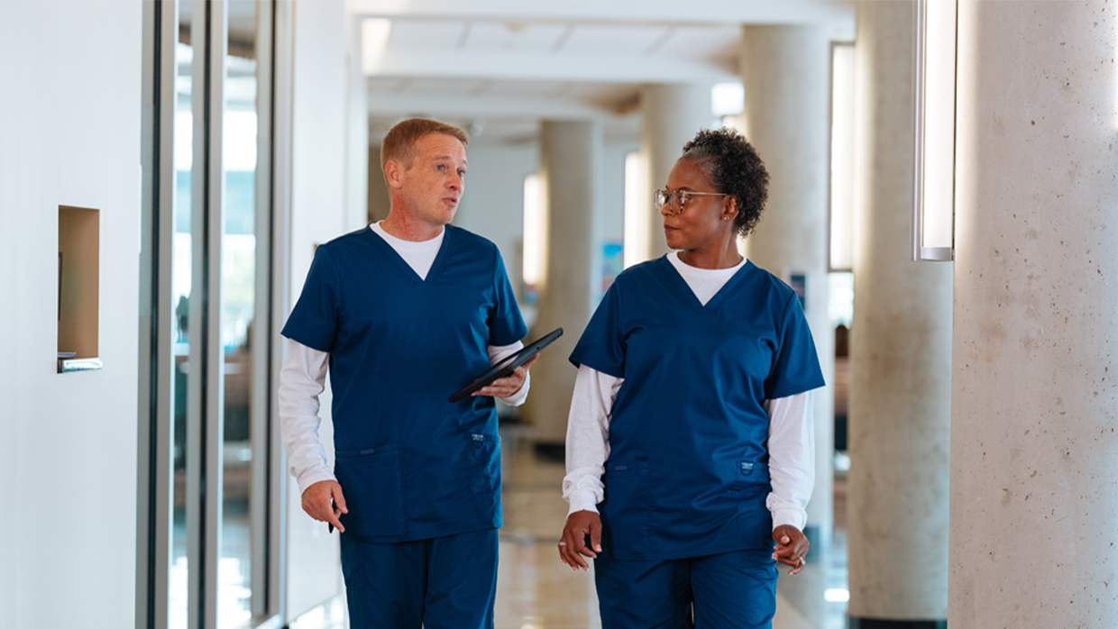 Two healthcare employees walking together down a hospital hallway
