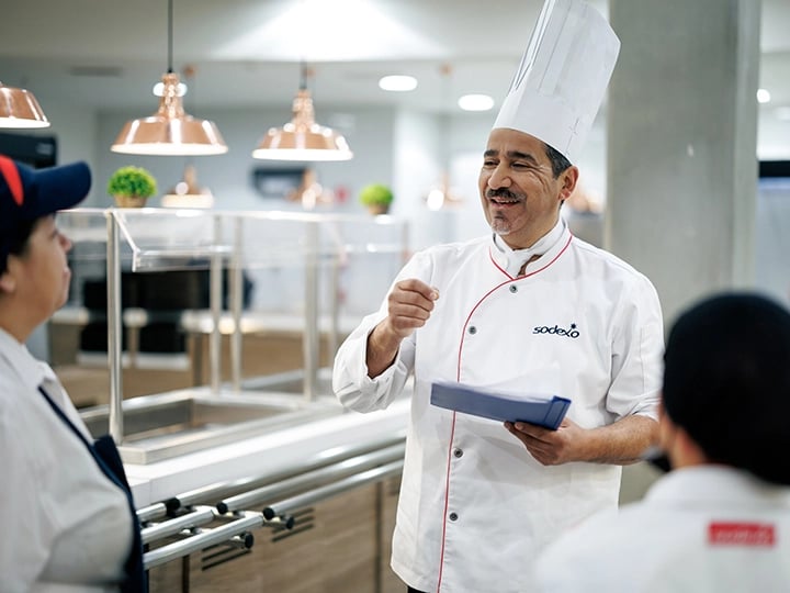 A man in a chef hat engages with a group of people, sharing culinary insights and tips.