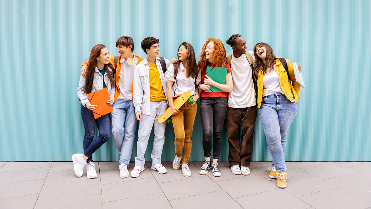 A diverse group of young people standing together, smiling and engaging in conversation outdoors.