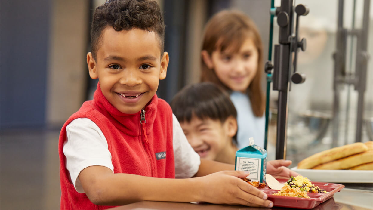 Three happy kids eating healthy meals at a school lunch table