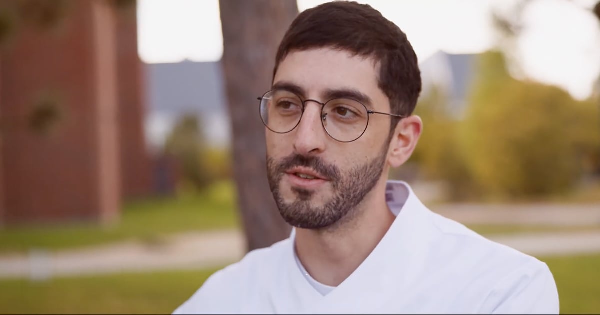 A man with glasses and a beard is gazing directly at the camera, presenting a thoughtful expression.