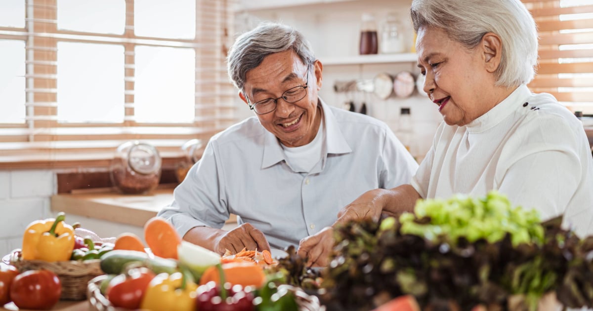Senior couple cooking together with fresh vegetables on the kitchen table.