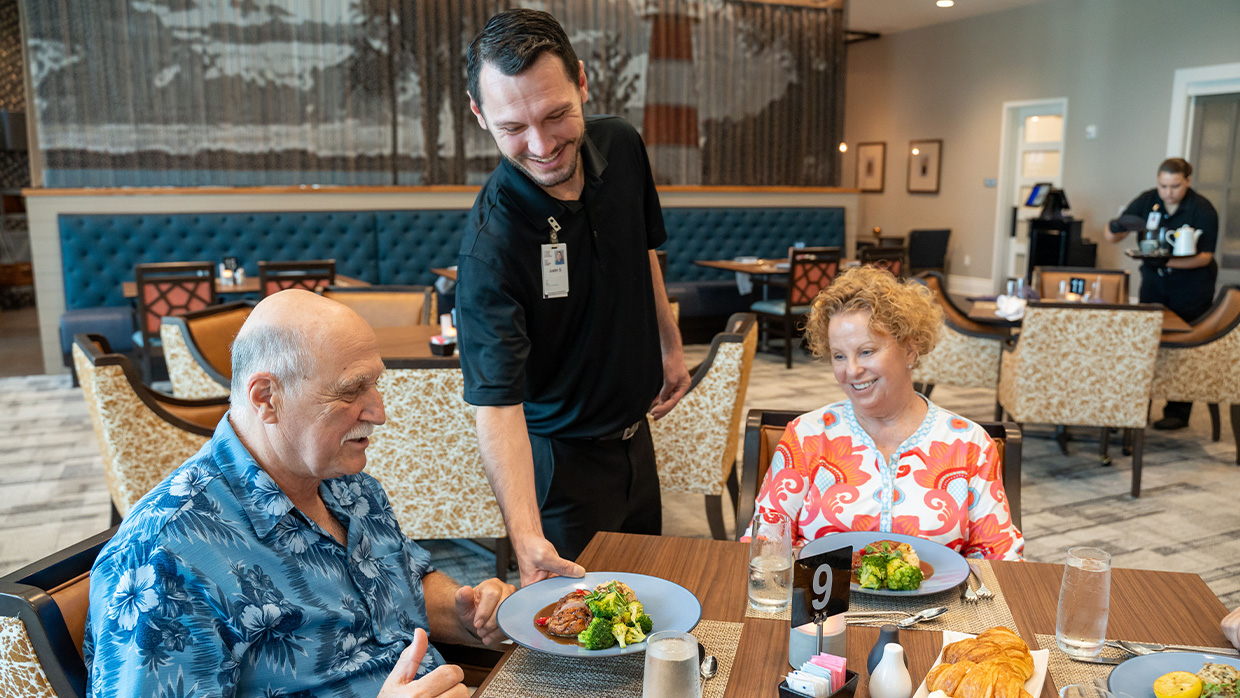 Server delivering plated meal to smiling senior couple in a dining setting