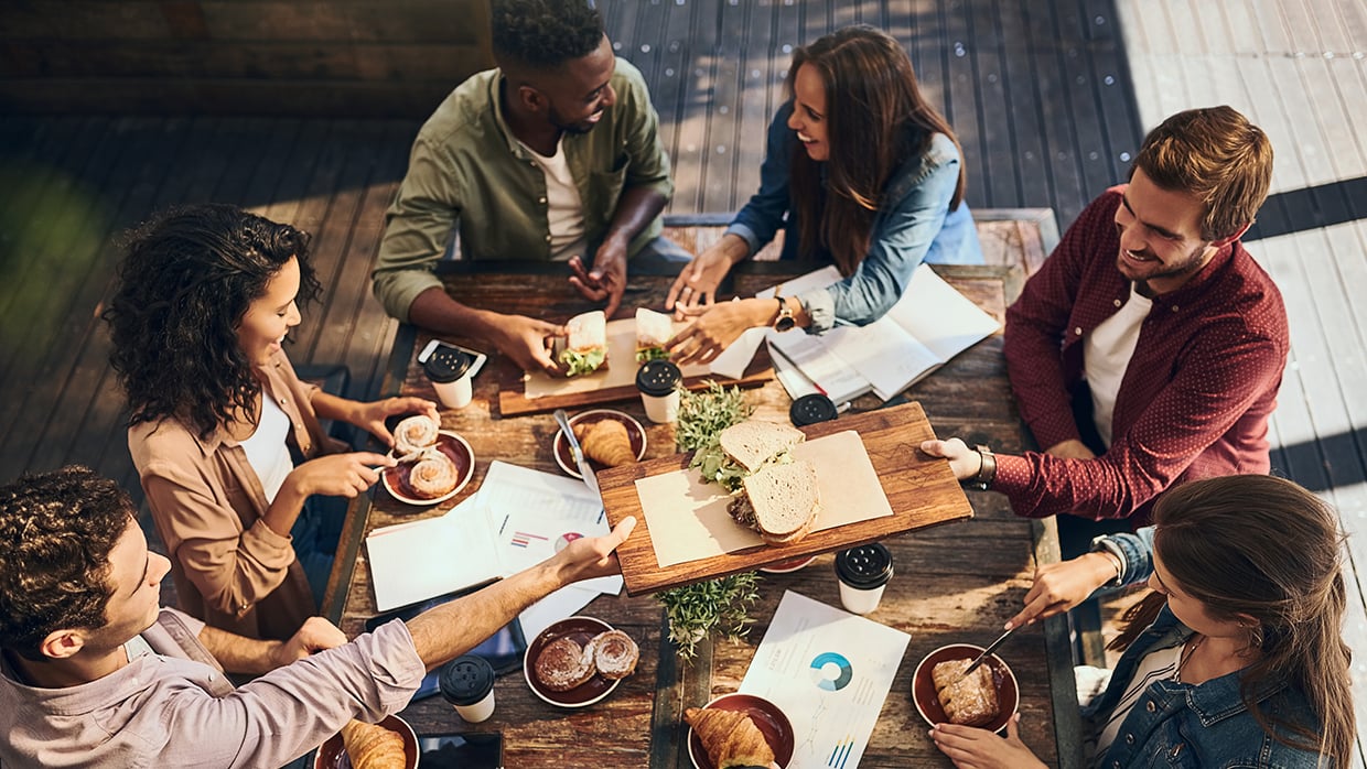 A diverse group of people gathered around a table, enjoying a meal together with various dishes and drinks.