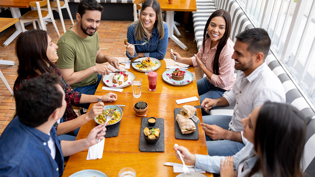 A group of diverse college students socializing and eating around a table