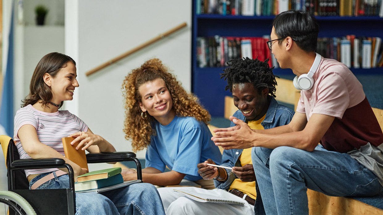 Group of happy college students engaged in a discussion together in a library.