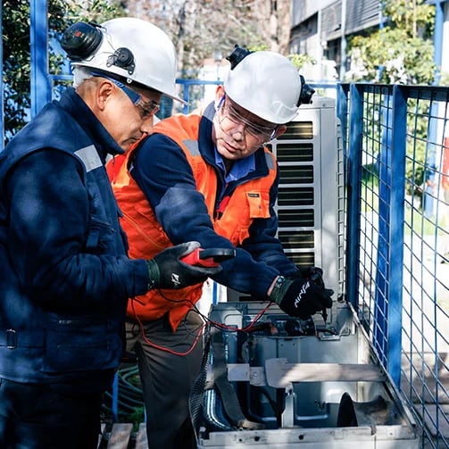 Two men in hard hats are collaborating on a piece of industrial equipment.
