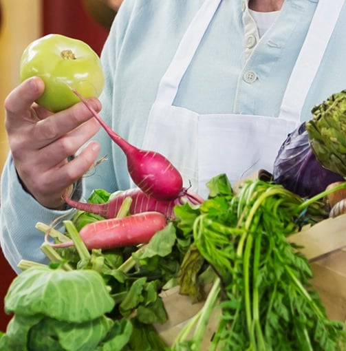 A man stands holding a basket filled with fresh vegetables, showcasing a variety of colors and types.