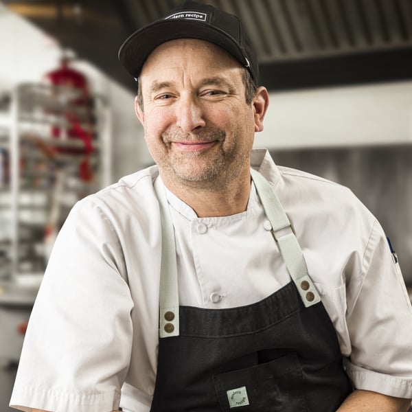 smiling chef wearing a black apron and cap in a professional kitchen