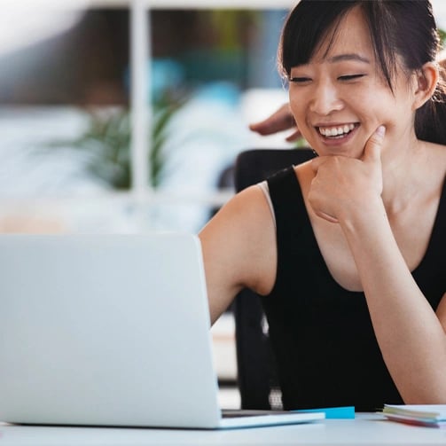 A woman sitting at a desk, focused on her laptop, with a notepad and pen beside her.
