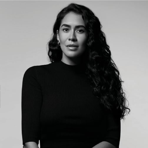 Black and white portrait of a person with long, wavy hair wearing a black, long-sleeved top, set against a plain light-colored background
