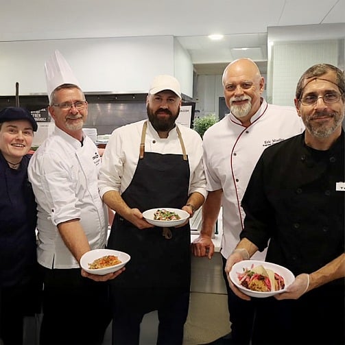 Chef Efrén Hernández with SUNY chefs presenting plated dishes in a campus kitchen. 