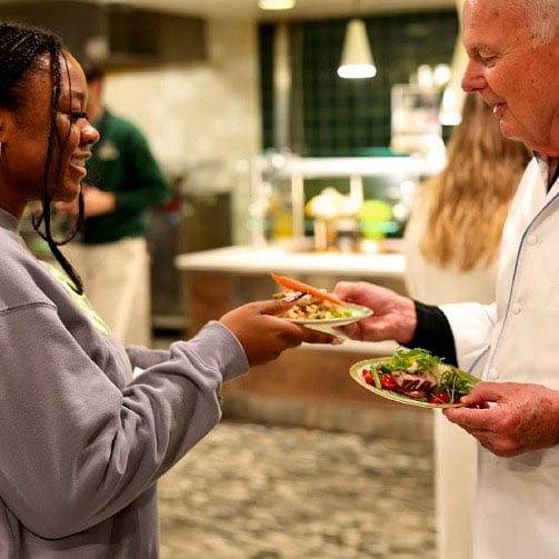 Chef personally serving a salad dish to a student in a campus dining hall. 