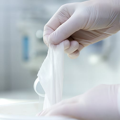 Gloved hands pulling a disinfectant wipe.