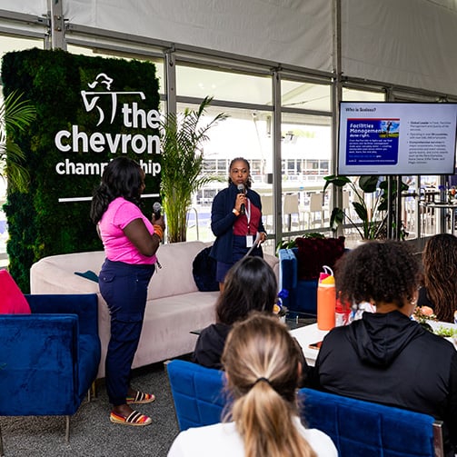 Speaker presents to seated attendees at The Chevron Championship lounge with presentation screen in background.