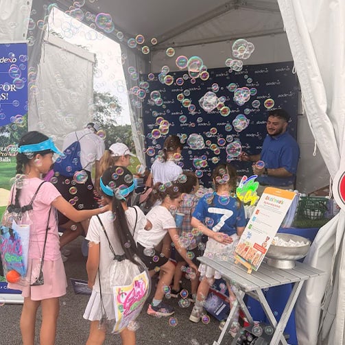 Children gather at a bubble activity booth inside an event tent, surrounded by floating bubbles.