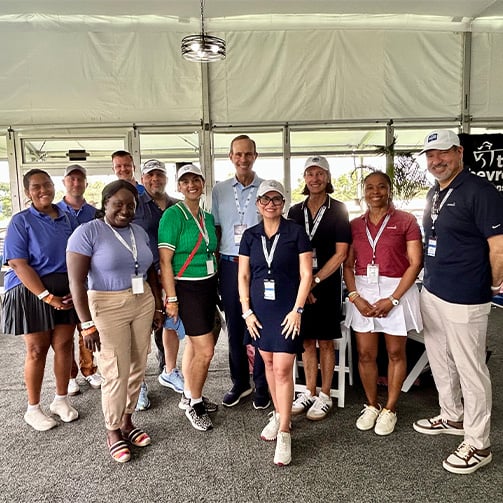 Group of event attendees pose together inside a hospitality tent at a golf tournament venue.