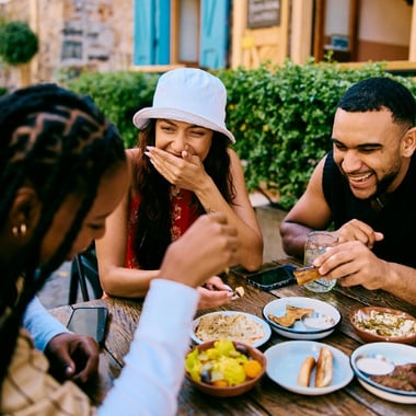 Three college friends laughing together over a shared meal outdoors.