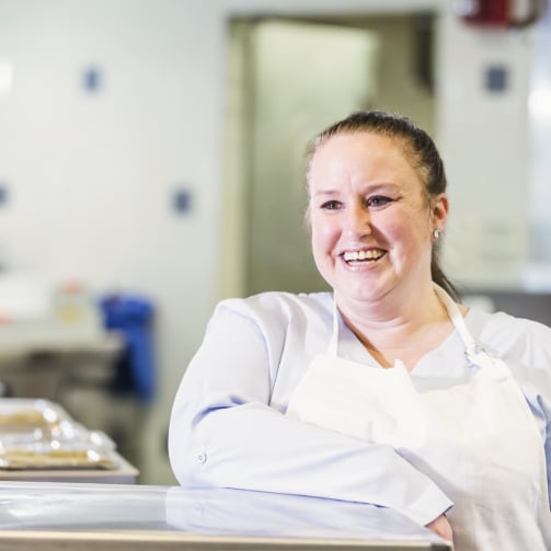 A dining hall staff member standing in the kitchen with a bright smile.