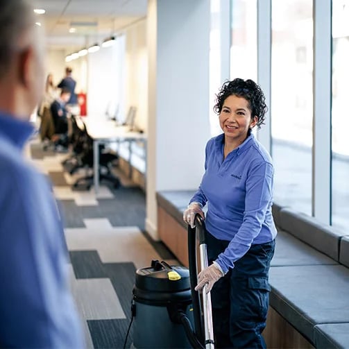 A woman wearing a blue shirt and gloves is cleaning a vacuum cleaner.