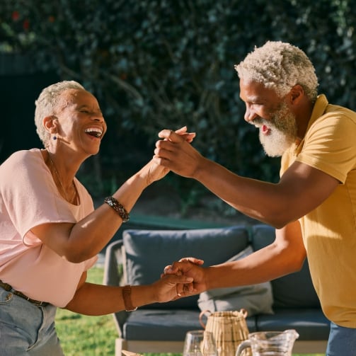 A senior couple dancing hand in hand in an outdoor setting, enjoying a joyful, carefree moment together.