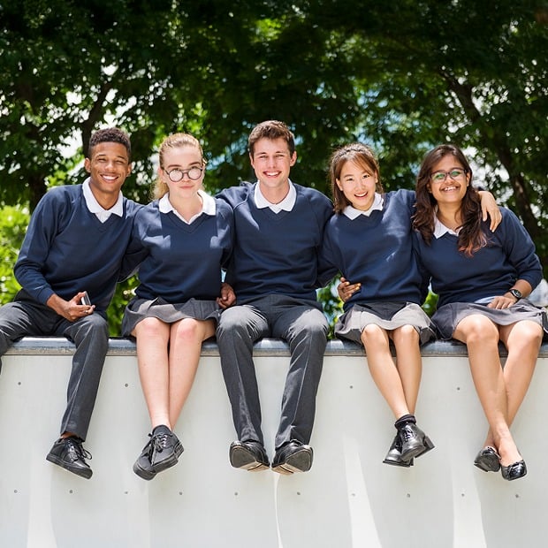 Students in uniform sit close together on a stoop with their arms around each other, trees behind them.