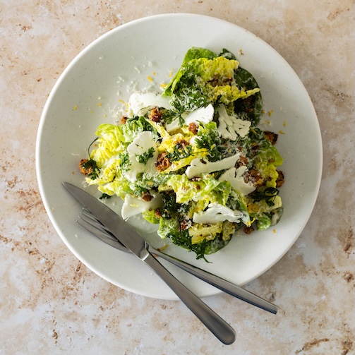 Top-down view of Caesar salad with romaine, dressing, cheese, and croutons, with fork and knife on a plate.