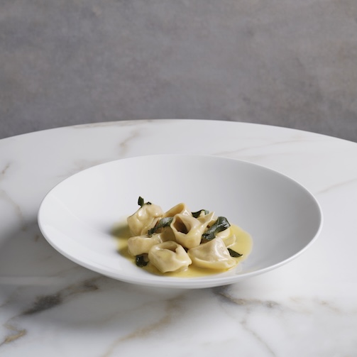 Small serving of tortellini in a creamy sauce on a white plate set on a marble table.