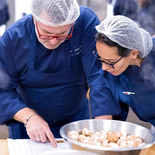 Two people in a kitchen examining a bowl of fresh mushrooms on a countertop.