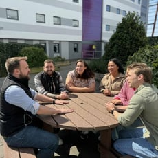 Group of interns gathered closely around a table, engaged in a lively discussion.