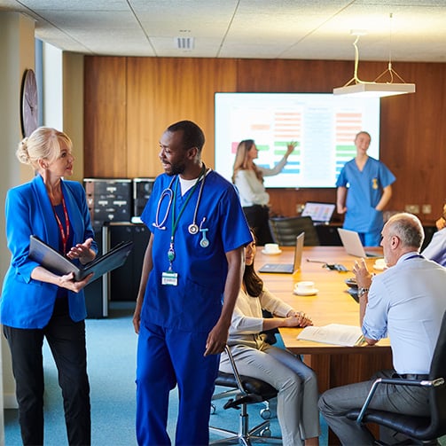 Healthcare staff and administrators collaborating in a meeting room during a presentation on performance metrics.
