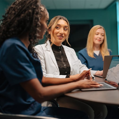 Healthcare professionals collaborating around a conference table, using laptops during a team meeting.