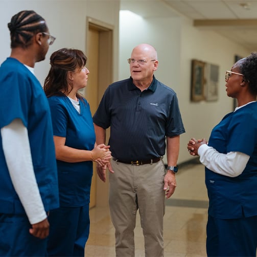 Healthcare staff and administrator conversing in a hospital hallway during a team discussion.