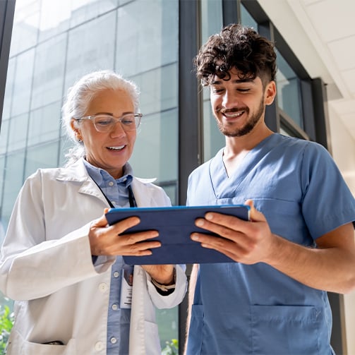 Healthcare colleagues reviewing information on a tablet in a bright hospital or clinic corridor.