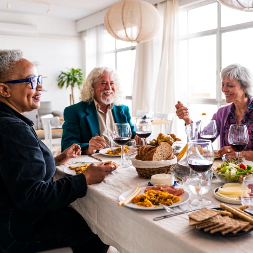 A group of seniors sitting around a dining table, smiling and laughing as they enjoy a meal together.