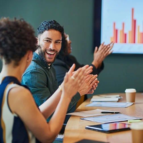 A diverse group of people clapping enthusiastically during a meeting, showing support and engagement.